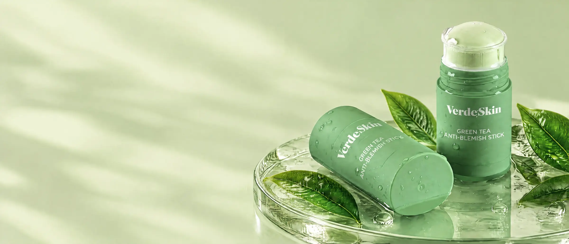 Two VerdeSkin green tea sticks on a glass dish with fresh tea leaves